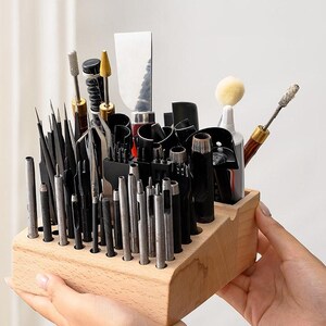 May include: A wooden organiser with a variety of leather crafting tools, including punches, awls, and a scraper. The organiser has multiple slots to hold the tools upright.