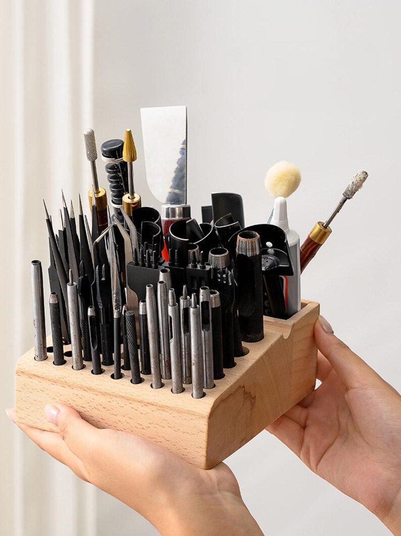 May include: A wooden organiser with a variety of leather crafting tools, including punches, awls, and a scraper. The organiser has multiple slots to hold the tools upright.