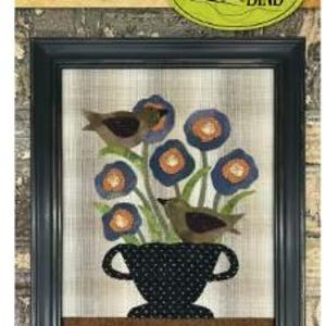 May include: Framed wool applique artwork titled "Spring Centerpiece." The image features a black vase with a floral arrangement of blue flowers and two brown birds. The artwork is framed in a black wooden frame and measures 11.75 x 14 inches. The text "Threads that Bind" is in the upper right corner.