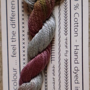 May include: A skein of stranded cotton embroidery floss in shades of gray, burgundy, and olive green. The label indicates 100% cotton, hand-dyed in Australia, and 50cm lengths.