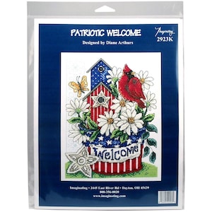 May include: Cross stitch pattern featuring a red cardinal perched on a birdhouse with red, white, and blue patriotic colors. The birdhouse is surrounded by white daisies and a welcome sign. The pattern is titled "Patriotic Welcome" and is designed by Diane Arthurs.