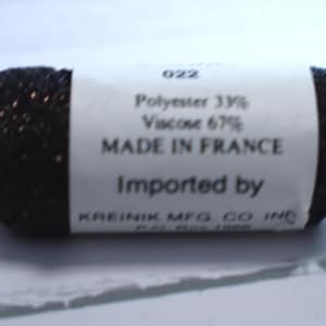 May include: A spool of black thread with a white label. The label reads "Polyester 33% Viscose 67% MADE IN FRANCE Imported by KREINIK MFG CO INC". The thread is wrapped around a white spool.