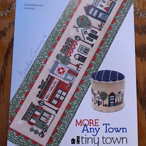 May include: A cross-stitch kit with a town scene, featuring buildings, trees, and the text "MORE Any Town tiny town." Includes a matching pin cushion. The kit is from "HEART IN HAND needleart."