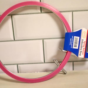 May include: A bright pink embroidery hoop with a silver metal clasp. The hoop has a tag that reads "Spring Tension Embroidery Hoop". The hoop is 5 inches in diameter.