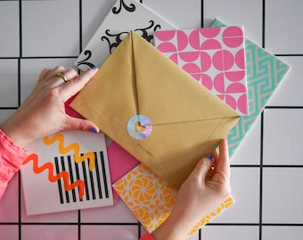 May include: A stack of colorful patterned paper with a brown envelope on top. The envelope has a heart-shaped sticker on the front.