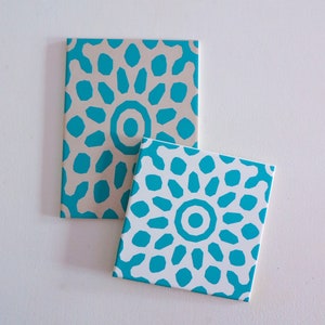May include: Two square notebooks with a geometric pattern. The top notebook has a beige background with a turquoise blue pattern. The bottom notebook has a white background with a turquoise blue pattern.