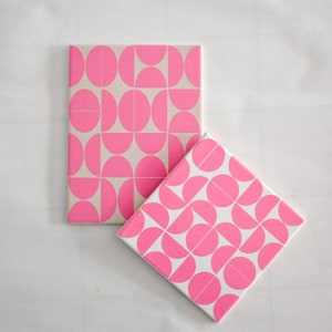 May include: Two square canvases with a geometric pattern of pink circles and semi-circles on a white background.