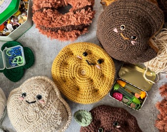 Könnte beinhalten: Eine Sammlung von gehäkelten Plüschtieren mit Essensthema, darunter ein Donut, ein Keks, eine Kartoffel und ein Schokoladenchip-Keks. Die Plüschtiere sind alle braun, beige, gelb und braun und haben süße Gesichter.