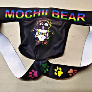May include: Black jockstrap with a rainbow "MOCHII BEAR" waistband and a colorful cartoon bear graphic. The straps are white and black with paw print designs.