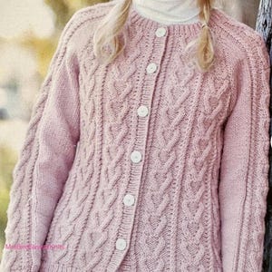 Könnte beinhalten: Hellrosa Strickjacke mit Zopfmuster und Knopfleiste. Der langärmlige Pullover hat ein strukturiertes Muster und einen runden Ausschnitt. Weiße Knöpfe verschließen das Kleidungsstück. Das Garn scheint weich zu sein.