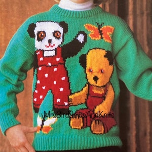 Puede incluir: Un suéter verde tejido con un oso panda con peto rojo y un oso de peluche con peto rojo. También hay una mariposa naranja y amarilla en el suéter. El suéter lo lleva una persona joven con cabello rubio y una diadema roja.