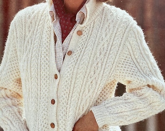 May include: A white cable knit cardigan with wooden buttons and pockets. The cardigan is worn over a white button-down shirt with a red patterned scarf.