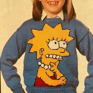 May include: A blue knitted sweater with a yellow cartoon character of Lisa Simpson from The Simpsons. The character is wearing a red dress and has a yellow star on her head.