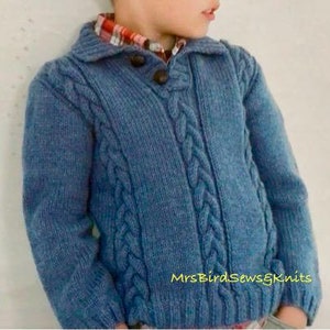 Peut inclure: Un pull bleu en tricot avec un motif en câble et un col boutonné. Le pull est pour un enfant, taille 46-71 cm.