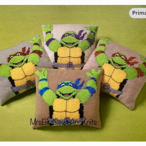 May include: Four square decorative cushions featuring Teenage Mutant Ninja Turtles. Each cushion has a different coloured mask, with green faces, yellow chests, and brown shells. The cushions are on a green surface, with the text "MrsBirdSewsAndKnits".