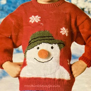 May include: Red knitted sweater with a snowman design. The snowman has a green hat, white face, and orange nose. The sweater has a snowflake design on the chest.