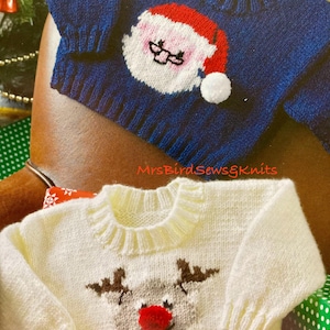 May include: Two knitted baby sweaters, one blue with a Santa Claus design and one white with a reindeer design.