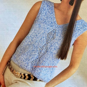May include: A blue and white sleeveless knitted top with a diamond pattern. The top is worn with a silver belt with a wavy design.