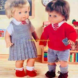 May include: Two knitted doll outfits for a boy and girl. The girl's outfit is a grey dress with a white collar and red stripes. The boy's outfit is a red sweater with a white collar and grey stripes, grey shorts, and grey socks. Both outfits have red shoes.