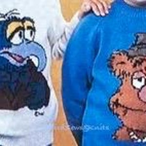 May include: Two knitted sweaters featuring characters from the Muppets. The sweater on the left is white with a blue and brown image of a blue bird with a bow tie. The sweater on the right is blue with a brown image of a bear wearing a hat.