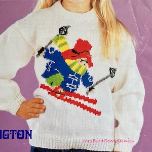 Op de afbeelding: Witte gebreide trui met een kleurrijk cartoon-skiër ontwerp. De skiër draagt een rode muts, een blauw jack, een groene broek en een gele en groene sjaal. De trui heeft de tekst "Mrs. Bird Sews & Knits" onderaan.