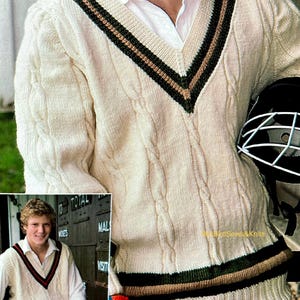 May include: Cream-colored cricket sweater with a V-neck and cable knit design. The sweater features green and brown stripes along the neckline and hem. A person is wearing the sweater and holding a cricket helmet.
