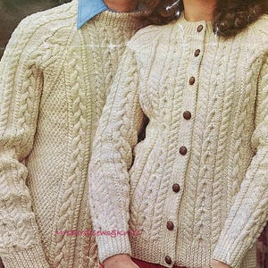 Puede incluir: Dos suéteres de punto de cable de color crema, uno un cárdigan con botones y el otro un jersey de cuello redondo.