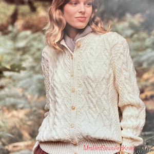 May include: A white cable knit cardigan with a button closure. The cardigan is worn by a person standing in a forest setting. The text "MrsBirdSewsandKnits" is visible on the bottom right of the image.