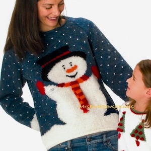 Peut inclure: Un pull en tricot bleu et blanc avec un motif de bonhomme de neige. Le bonhomme de neige porte un chapeau noir, une écharpe rouge et des mitaines orange. Le pull a un motif de flocon de neige blanc. Le texte "DESIGN 5 ARAN 8" est visible dans le coin supérieur droit de l'image.