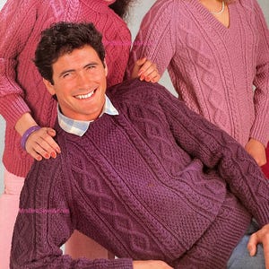Könnte beinhalten: Eine Gruppe von Personen trägt Strickpullover in Rosa- und Lilatönen. Die Pullover weisen Zopfmuster und strukturierte Muster auf. Der Mann im Vordergrund trägt einen dunkelvioletten Pullover mit einem Hemd mit Kragen darunter.