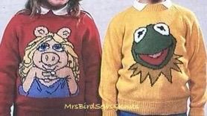 May include: Two knitted sweaters featuring cartoon characters. The sweater on the left is red with a pink pig wearing a blue dress. The sweater on the right is yellow with a green frog wearing a yellow shirt.