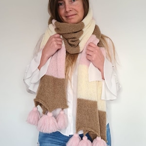 May include: A striped knit scarf with brown, pink, and white stripes and pink pom-poms on the ends.