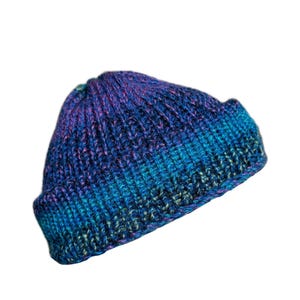 May include: A hand-knitted beanie hat in shades of blue and purple. The hat features a ribbed knit design and a folded brim. The colors blend together, creating a gradient effect. This winter hat is a cozy accessory.