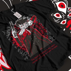 May include: Black t-shirt with a white graphic of a character holding two guns. The text "The bird of Hermes is my name, eating my wings to make me tame" and "SHINE HEAVEN" are printed on the shirt.