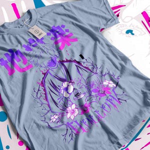Pode incluir: T-shirt azul claro com um design gráfico que incorpora caracteres japoneses e uma ilustração roxa e rosa. O design inclui elementos florais e a palavra "Hollow" em escrita cursiva.