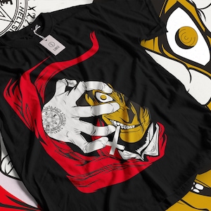May include: Black t-shirt with a red and white graphic of a character with a single eye, a cross, and a pentagram. The character is holding a cigarette in their mouth.