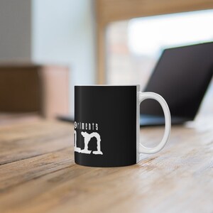 May include: A black ceramic mug with a white graphic that says "The Experiments" and "LM" in a stylized font.