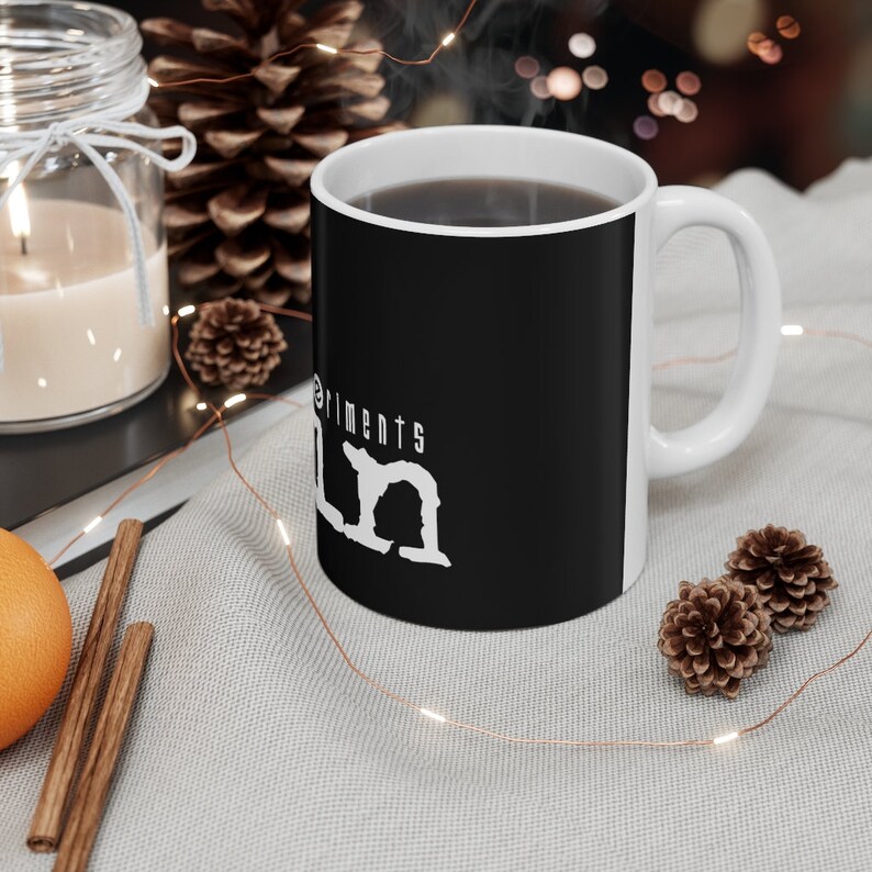 May include: A black ceramic mug with a white design that says "Experiments in Calm". The mug is filled with coffee and has steam rising from it.