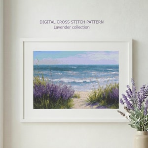 May include: A framed digital cross stitch pattern print from the Lavender collection. The artwork depicts a beach scene with lavender bushes, tall grass, and ocean waves. A vase of lavender sits on a wooden table.