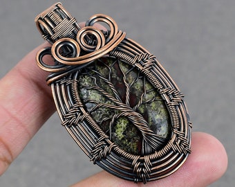 Könnte beinhalten: Ein mit Kupferdraht umwickelter Anhänger mit einem grün-braunen Baum des Lebens Stein. Der Anhänger ist oval geformt und hat eine Öse aus Kupfer.