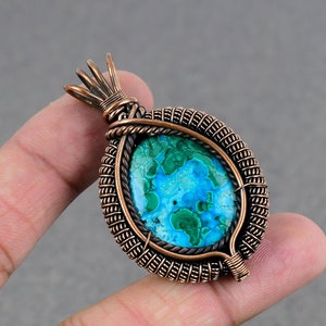 May include: A copper wire wrapped pendant featuring a green and blue gemstone. The pendant has a unique, intricate design.