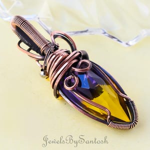 May include: A copper wire wrapped pendant featuring a faceted gemstone with a yellow and purple gradient. The pendant is a unique piece of jewelry.