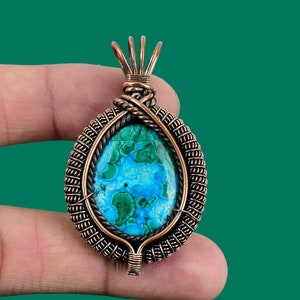May include: A copper wire wrapped pendant featuring a green and blue malachite stone. The pendant has a detailed wire design and is perfect for adding a touch of nature to any jewelry collection.