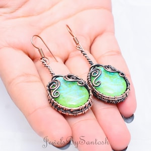 May include: A pair of copper wire wrapped earrings with green and blue iridescent glass cabochons. The earrings have a delicate, intricate design.