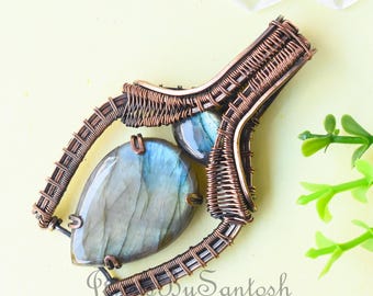 Peut inclure: Un pendentif en fil de cuivre enroulé avec deux pierres de labradorite irisées. Le pendentif a la forme d'une larme et présente un motif de fil tissé.