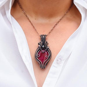 May include: A copper wire wrapped pendant necklace featuring a large, red gemstone. The pendant is shaped like a teardrop and has a silver accent at the top.