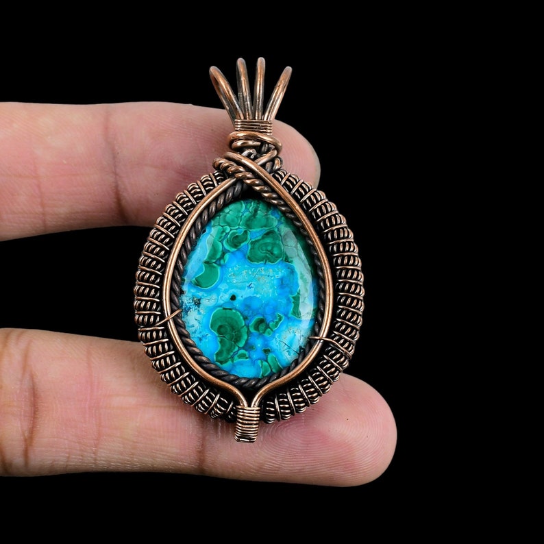May include: A copper wire wrapped pendant featuring a green and blue gemstone. The pendant is oval shaped and has a detailed wire design.