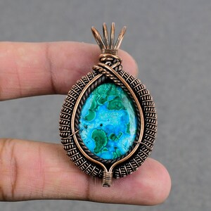 May include: A copper wire wrapped pendant featuring a green and blue malachite gemstone. The pendant has a woven wire design and a loop at the top for attaching a chain.