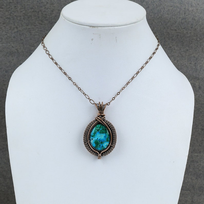 May include: A copper wire wrapped pendant necklace featuring a blue and green gemstone. The necklace is on a white display stand.