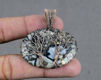 May include: A copper wire wrapped pendant featuring a tree of life design with a black and white agate stone. The stone has a unique pattern of white and black swirls.
